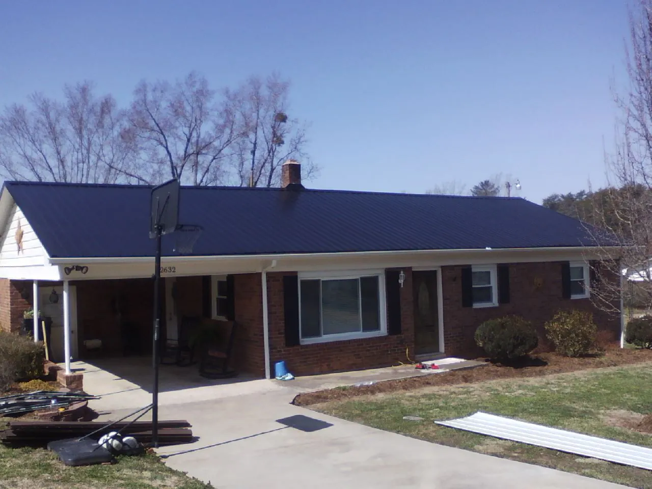 Finished dark blue metal roof on a brick ranch with a carport in Shawnee