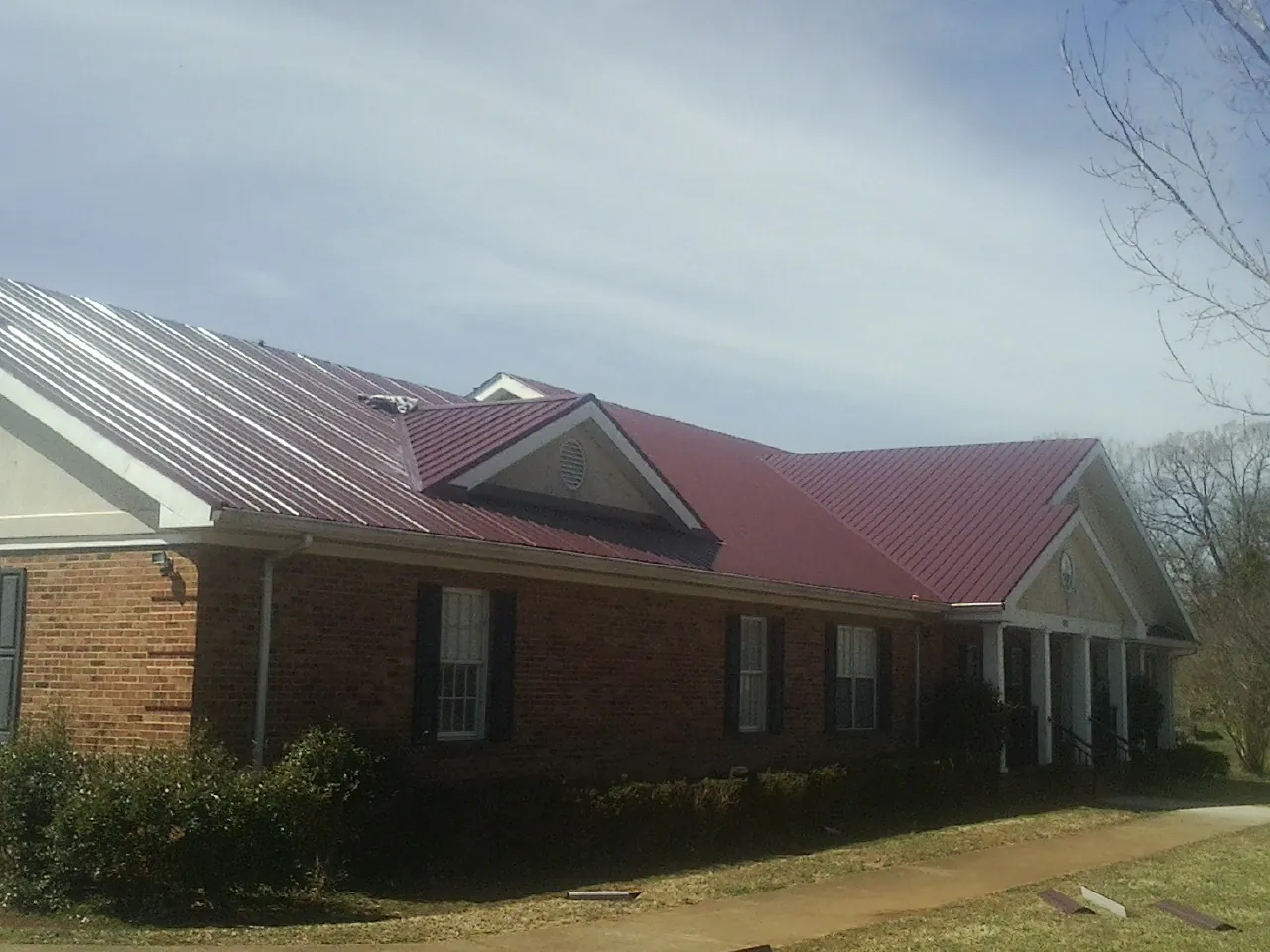Red metal roof with gabled entries on a long brick building, from a Hail Damage Roof Repair job in Shawnee