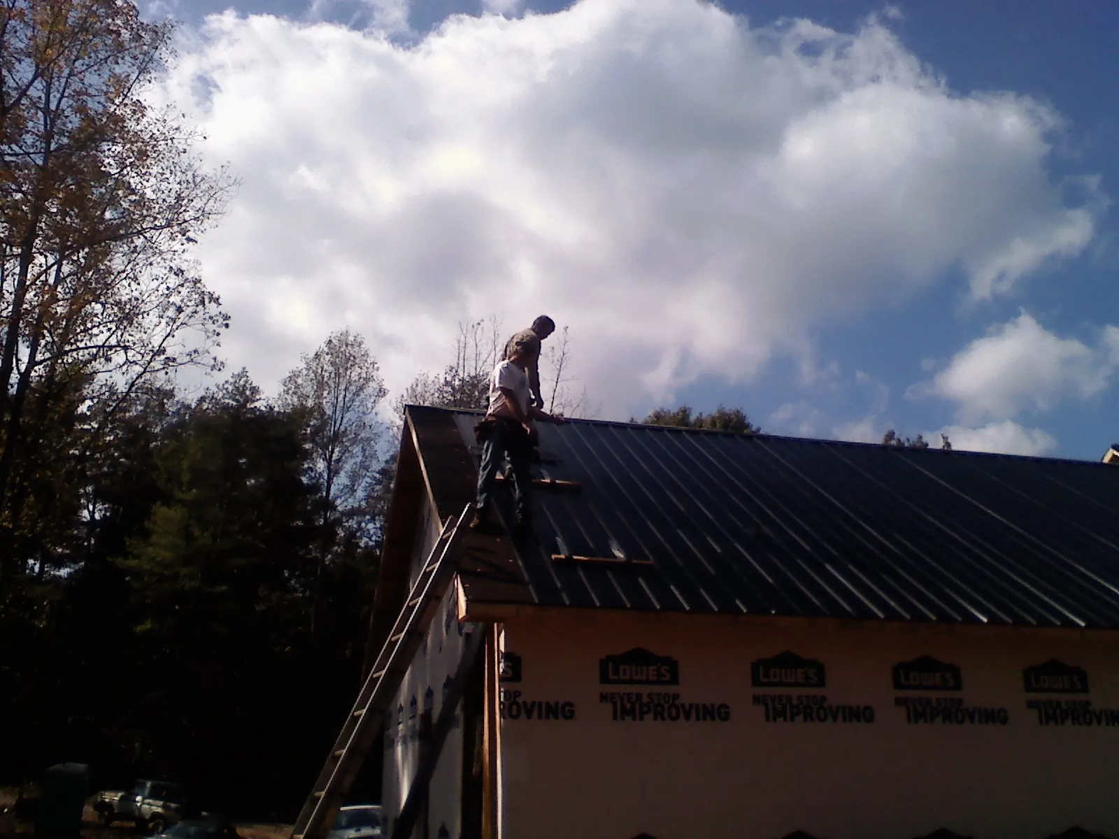 Roofer fastening dark metal panels high against a cloudy sky, from a Roof Inspection job in Shawnee